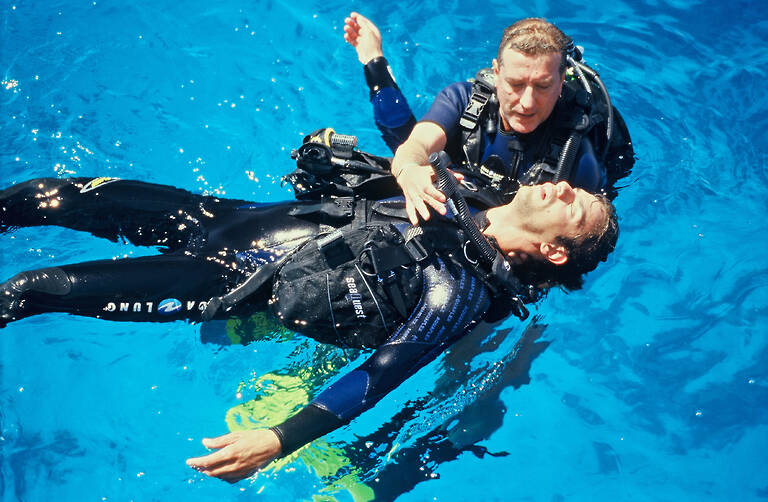 One diver rescuing another on the surface of the water